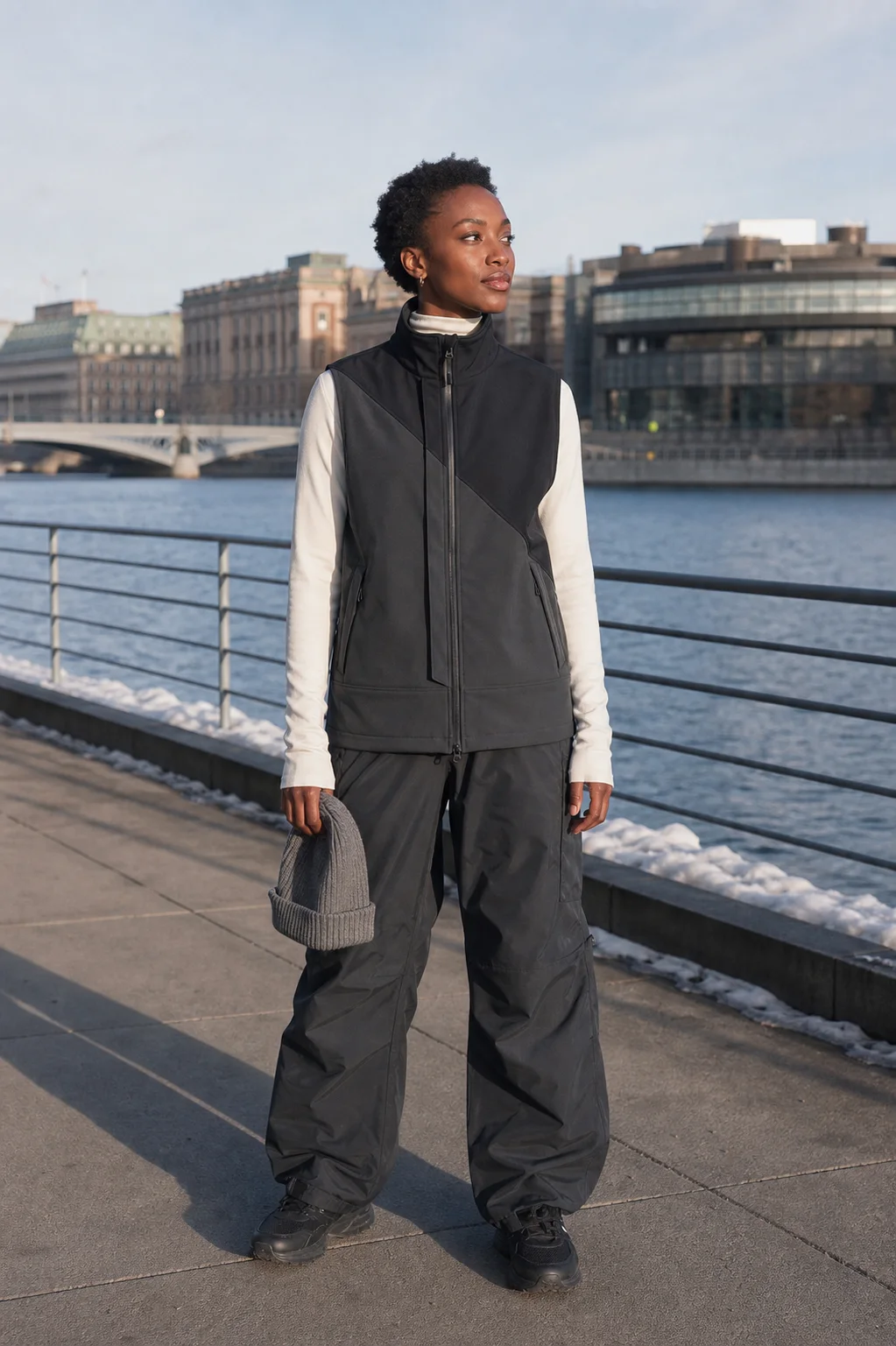 Stockholm waterfront styling image showing the Clothixpack CXP-A106 Kilo Waterproof Vest over a cream mock neck and black shell pants.